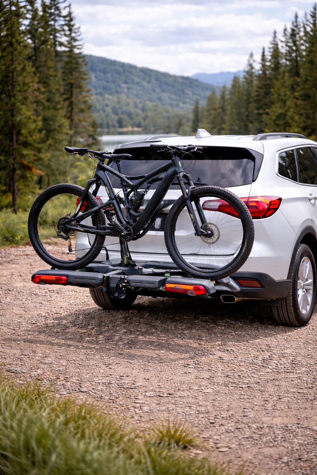 A bike mounted on the back of a white SUV on a forest road.